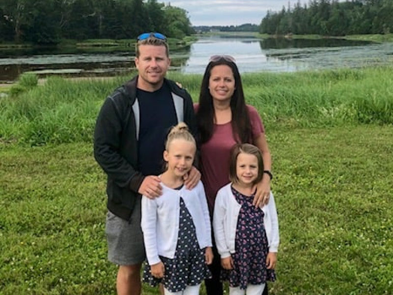 Carrie Nelson, a middle-aged woman, smiling with her husband and two young daughters in a field.