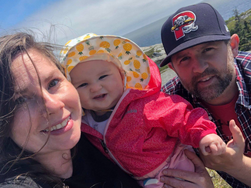 Jenn Dixon, her partner Shawn, and their daughter smiling outside on a sunny day