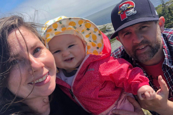 Jenn Dixon, her partner Shawn, and their daughter smiling outside on a sunny day